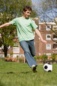 Full-length view of a teenage boy about to kick a soccer ball outdoors.