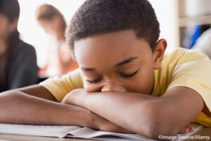 Close-up of African-American junior high school boy asleep in class with his head on his folded arms. ©Image Source/Alamy. MHE World.