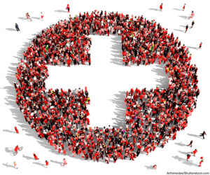 Large group of people dressed in red clothes gathered together in the shape of a plus sign.