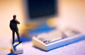 Miniature male figure standing on computer mouse.