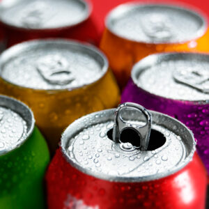 A view of the tops of six various soda cans with condensation. One of the cans in the foreground is open.