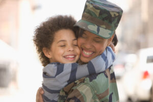 Head and shoulders selective focus view of a happy young mixed race woman, wearing in army fatigues, hugging her 4-5 year old son after returning home, West New York, NJ, USA