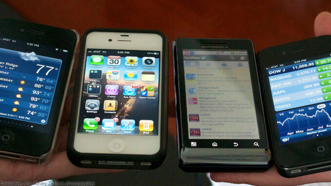FS_04P_112513 High-angle close-up view four smartphones displayed in a row across the palms of two human hands