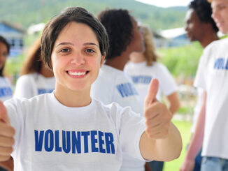 happy volunteer girl showing thumbs up sign group in background