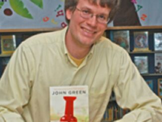 author John Green with his paperback novel Paper Towns