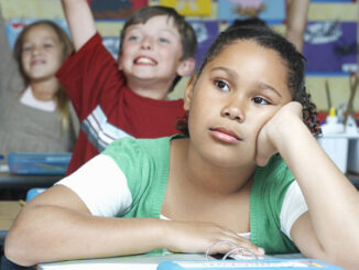 Three pupils in classroom, two with raised hands, one pensive. Photo: moodboard/Getty Images