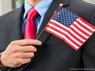 Man in a business suit holding a small American flag against his chest