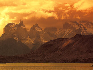 Rainy clouds over mountains by the sea at dusk. Photo: Glow Images