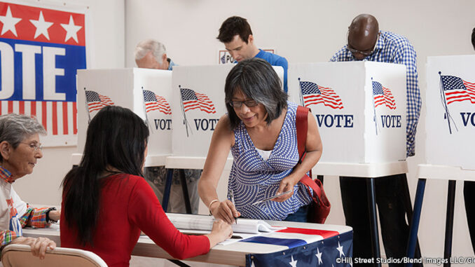 BLD091968 Three-quarter-length view of an Asian woman signing in to vote at a polling location, four men at voting booths behind her. MHE World.