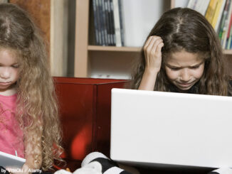 Full-length view of two confused pre-school age girls sitting side by side in a living room. Each girl is looking down and stratching her head while using a wireless computer device.© PEOPLE AND TECHNOLOGY by VISION / Alamy.World.