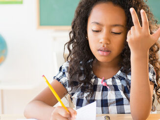 Head-and-shoulders view of a mixed-race girl counting on her fingers and writing in a notebook in class. ©JGI/Jamie Grill/Blend Images LLC. MHE World.