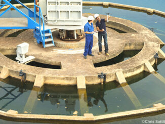 High angle full-length view of two Hispanic men standing on a platform and checking the water quality in a sewage treatment plant. ©Chris Sattlberger/Blend Images LLC. MHE World.