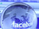 Selective focus close-up view of a small, transparent glass globe of the earth placed in front of a computer monitor displaying Facebook. The globe creates a fisheye magnification of the word 'facebook' on the screen. As of today, Facebook is the largest social media network on the web. ©dolphfyn / Alamy. MHE World