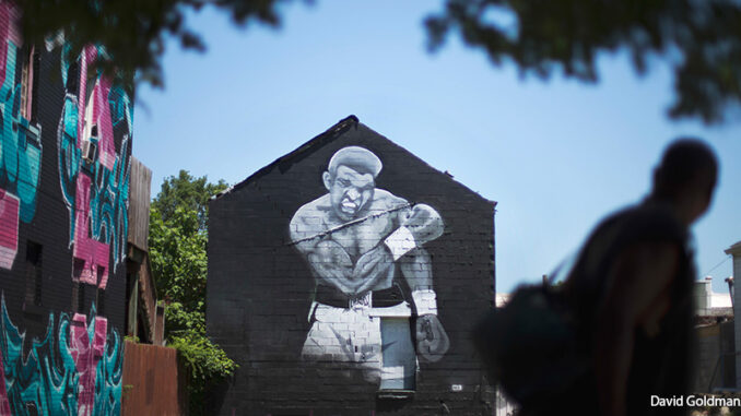 061516_02P_FS A pedestrian passes a mural of Muhammad Ali painted on the side of a building Monday, June 6, 2016, in Louisville, Ky.