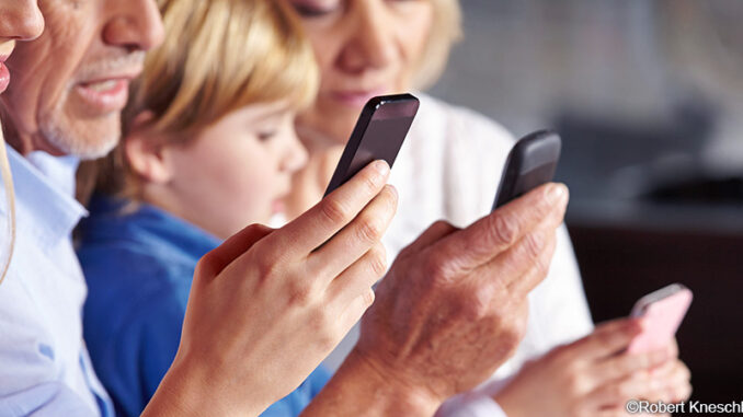 071916_02P_FS Waist-up, selective focus profile cropped view of four family members sitting side by side at the dinner table and using their smartphones. ©Robert Kneschke/Alamy. MHE World