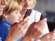 Waist-up, selective focus profile cropped view of four family members sitting side by side at the dinner table and using their smartphones. ©Robert Kneschke/Alamy. MHE World
