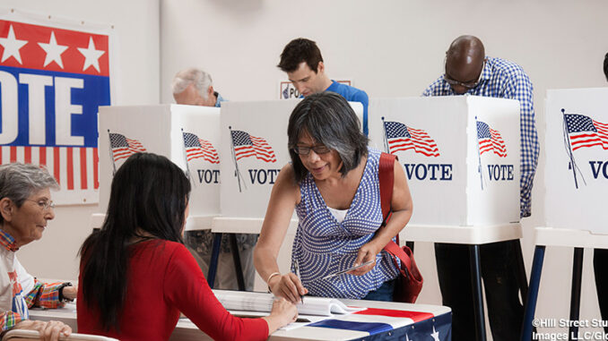 BLD091968 Three-quarter-length view of an Asian woman signing in to vote at a polling location, four men at voting booths behind her.