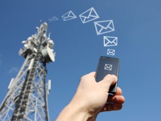 Man's hand holding a smart phone in front of telecommunication mast under a blue sky