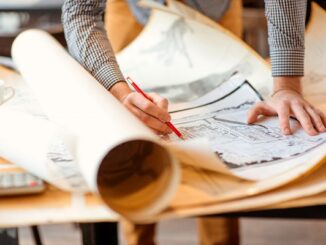Selective-focus close-up view of an urban planner with a couple of layers of architectural drawings on a drafting table. Credit: RossHelen/Shutterstock.com