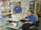 Three-quarter-length view of a Caucasian man with a disability, utilizing a wheelchair for mobility and enjoying time with a coworker in a retail store.