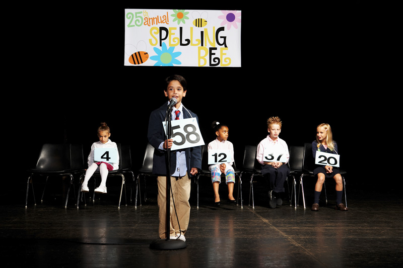 Children (6-9) on stage at spelling bee, boy at microphone