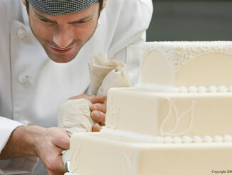 A man carefully decorating a wedding cake with lace icing details.