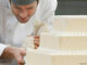 A man carefully decorating a wedding cake with lace icing details.