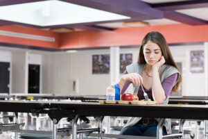 A student eats lunch in an empty cafeteria.