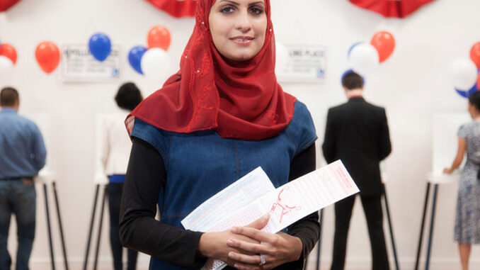 061318_02P_IS A young woman wearing a hijab at a voting location, holding a ballot.