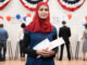 A young woman wearing a hijab at a voting location, holding a ballot.