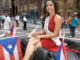 Miss Teen Princess, an hispanic female wearing a formal dress, waves a Puerto Rican flag while riding in a convertible car in a Puerto Rico Parade in New York City