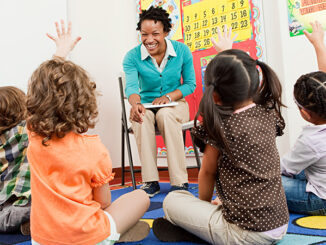 Teacher and children sitting on floors with hands raised