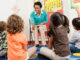 Teacher and children sitting on floors with hands raised