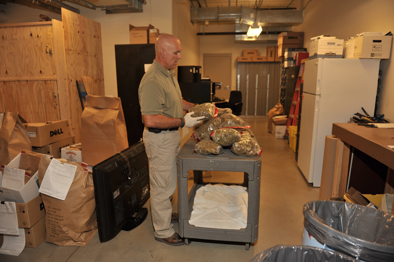 A police officer looking at bags of marijuana in a property room