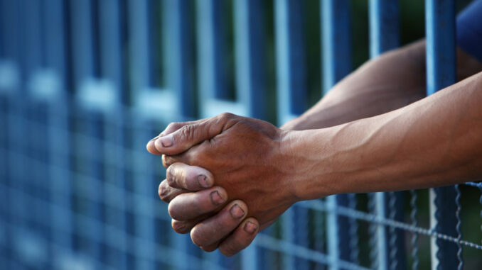 011419_01P_IS close-up view of hands clasping thru bars in a jail cell