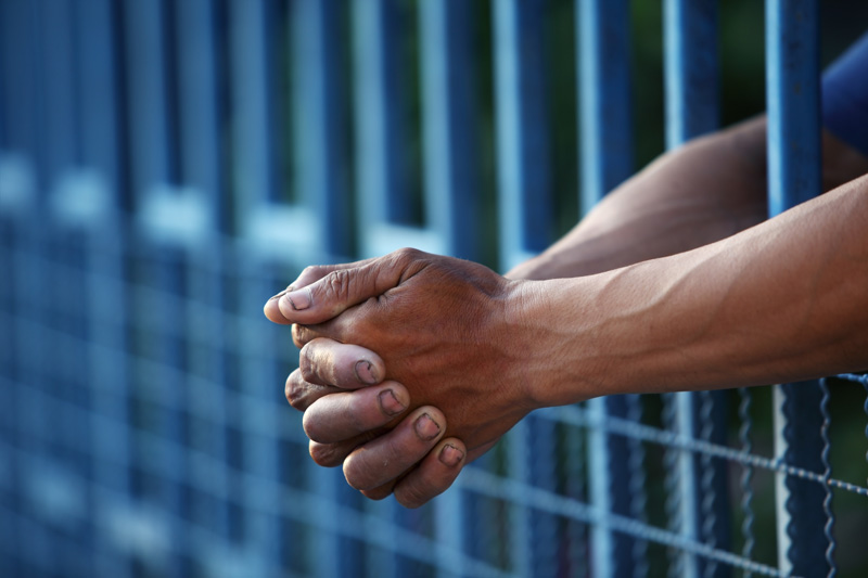 close-up view of hands clasping thru bars in a jail cell