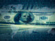 Image of a $100 bill in front of a digitized background with a world map