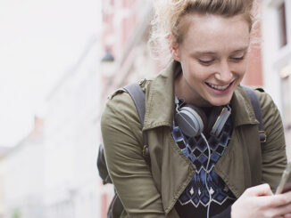 Smiling young woman texting with cell phone on bicycle on city street