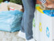 Close-up of person putting plastic bottles into bin with blue symbol