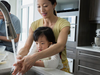 Mother and daughter washing hands in kitchen sink