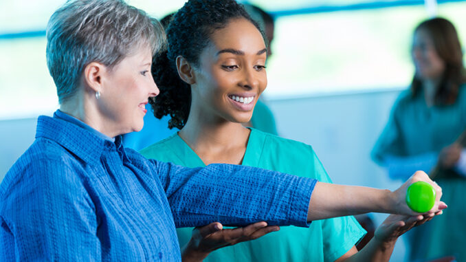 Professonial hospital physical therapist assisting senior woman with exercise Friendly physical therapist assisting senior patient with strength exercise