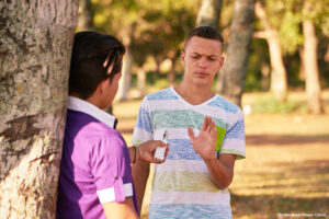 Waist-up selective focus view of a confident teenage boy refusing his friend's offer to smoke an electronic cigarette