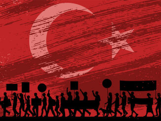 silhouetted image of marching protesters with signs in front of a full background image of the Turkey national flag