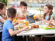 Children sitting at cafeteria table while eating lunch