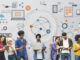 group of multicultural men and women on digital devices in front of a wall of digital images and computer-based icons