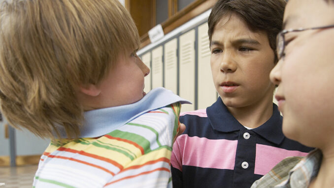 Schoolboy being bullied two 8-9 year old boys grabbing another boy's shirt collar in a school hallway