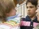 two 8-9 year old boys grabbing another boy's shirt collar in a school hallway