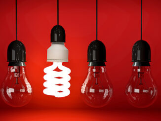Glowing eco saving bulb hanging on wire in row of incandescent bulbs over red background