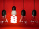 Glowing eco saving bulb hanging on wire in row of incandescent bulbs over red background