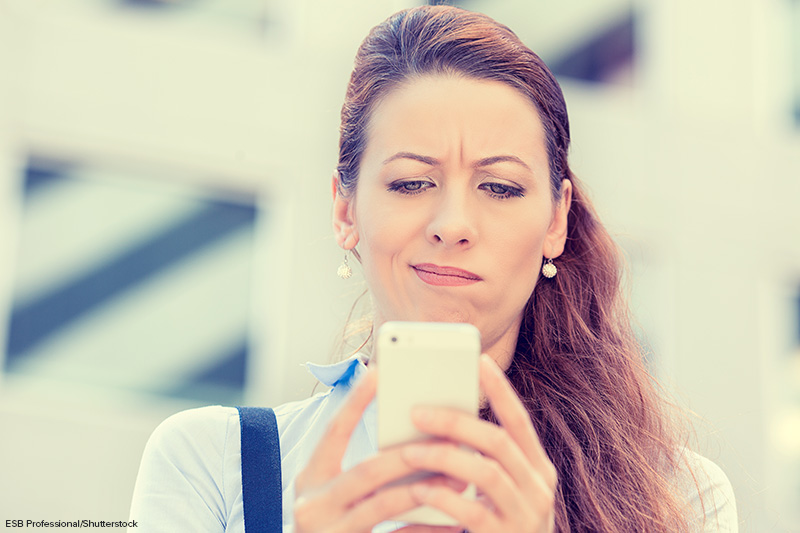 Low angle, selective focus, head and shoulders view of an annoyed woman holding a smart phone and looking down at the screen